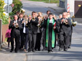 Pastorin, Posaunenchor und Kinder mit Erntekrone und Erntegaben marschieren vom Pfarrhaus zur Kirche